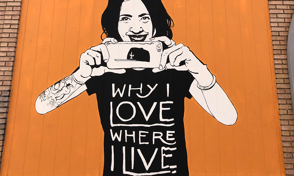 Woman holding smart phone with shirt saying "Why I love where I live"