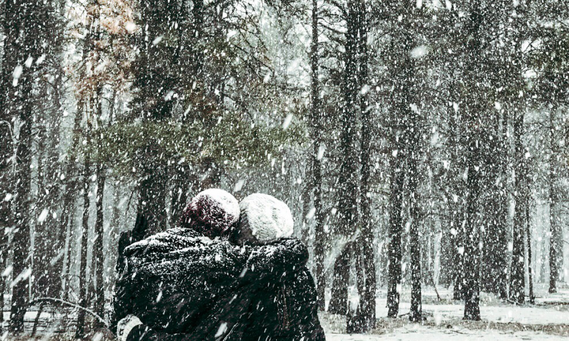 Two people hugging in the forest while it snows